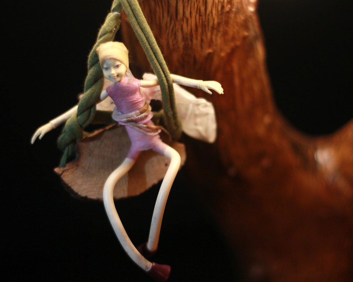 Detalle de figura de hada sentada sobre una lámpara de madera natural.